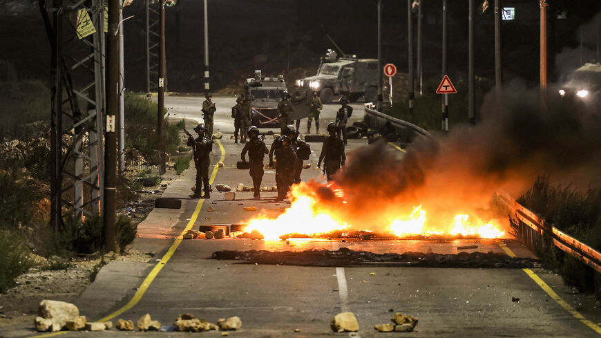 Israeli security forces stand behind a makeshift barricade of flaming tires separating them from Palestinian youths during clashes at the northern entrance of Ramallah, West Bank, Oct. 3, 2022.